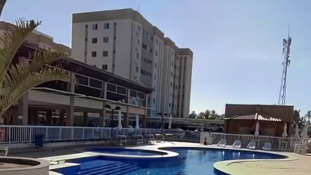 Una piscina bajo un cielo iluminado por el sol, una palmera y un edificio al fondo.
