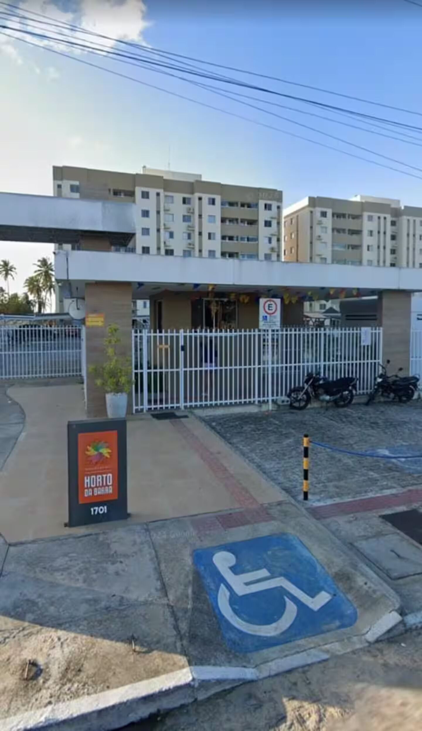 A hotel entrance with a wheelchair-accessible parking space, a sign for 'Horto da Barra', and a gated parking area.