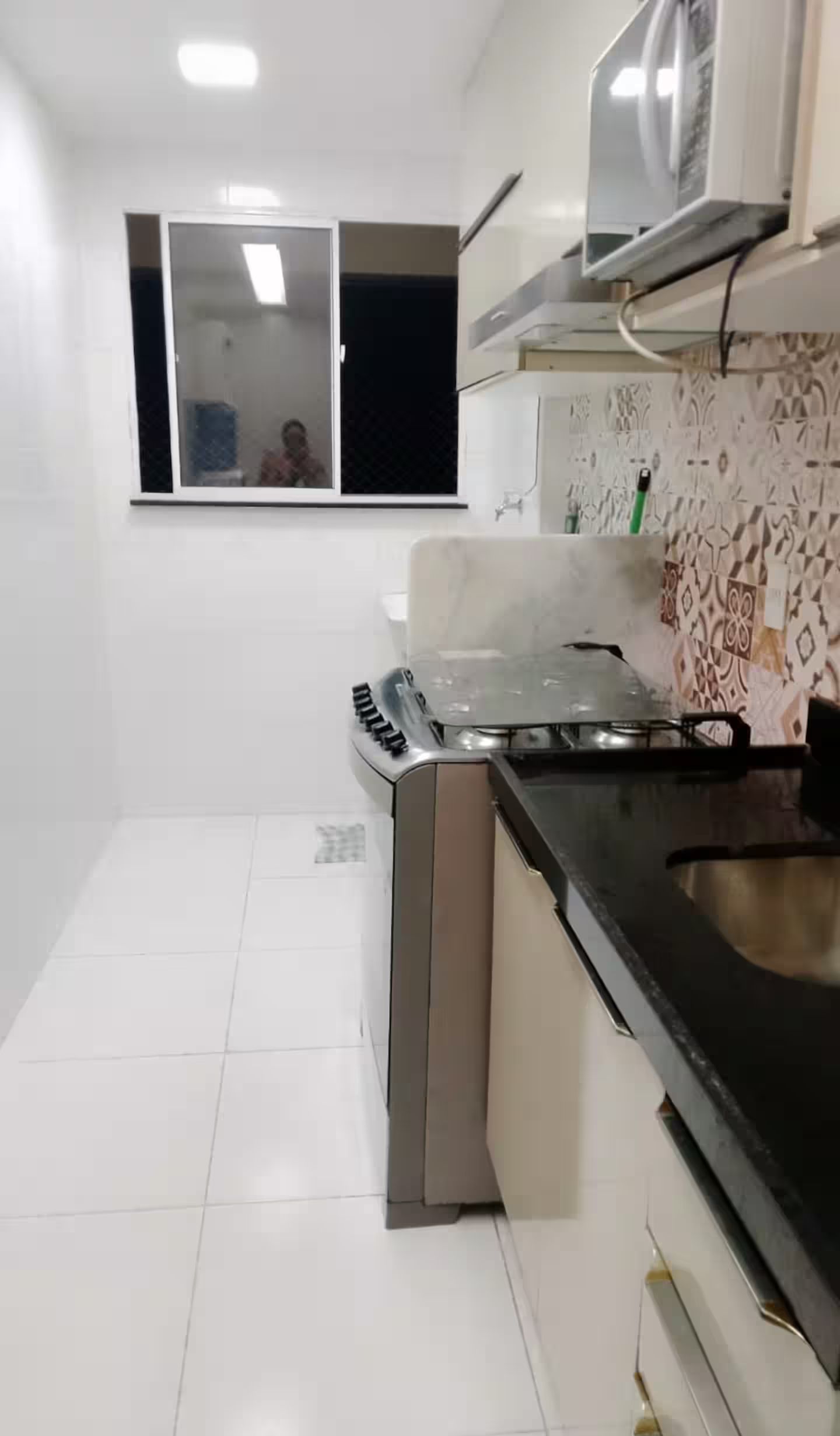 Een kleine keuken met witte tegels, een gasfornuis en een magnetron.