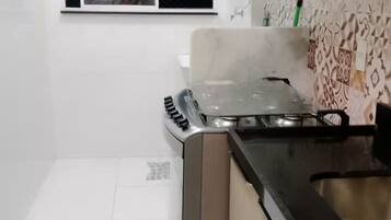 Een kleine keuken met witte tegels, een gasfornuis en een magnetron.