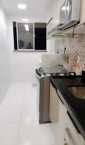 Una cocina compacta con baldosas blancas, cocina a gas y microondas.
