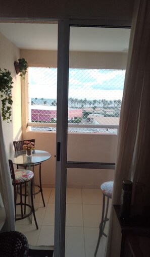 Un balcón con puerta de vidrio, una mesita con una silla y una planta en maceta.
