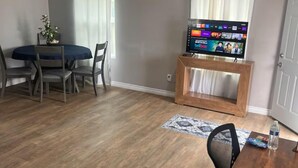 A living room with a dining area, a TV on a wooden stand, and a small rug. - Spacious and Private (Bakersfield)