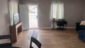 A spacious living room with a wooden floor, a blue sofa, a dining table with chairs, and a view through a glass door to the outside. - Spacious and Private (Bakersfield)