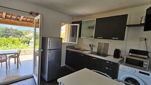 A compact kitchen with a refrigerator, microwave, and washing machine, a dining area with chairs, and a view of greenery outside. - T2 Dolce & Vita B3 with pool (Propriano)