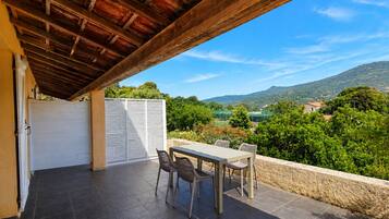 Une terrasse couverte avec une table et des chaises, une vue sur un paysage montagneux et une clôture blanche.