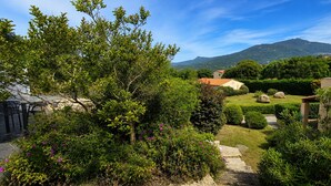 A garden with a stone path leading to a house with a red roof, surrounded by greenery and a mountain in the background. - T2 Dolce & Vita B3 with pool (Propriano)