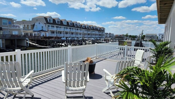 A deck with white Adirondack chairs, a railing, and a view of a marina with boats and houses.