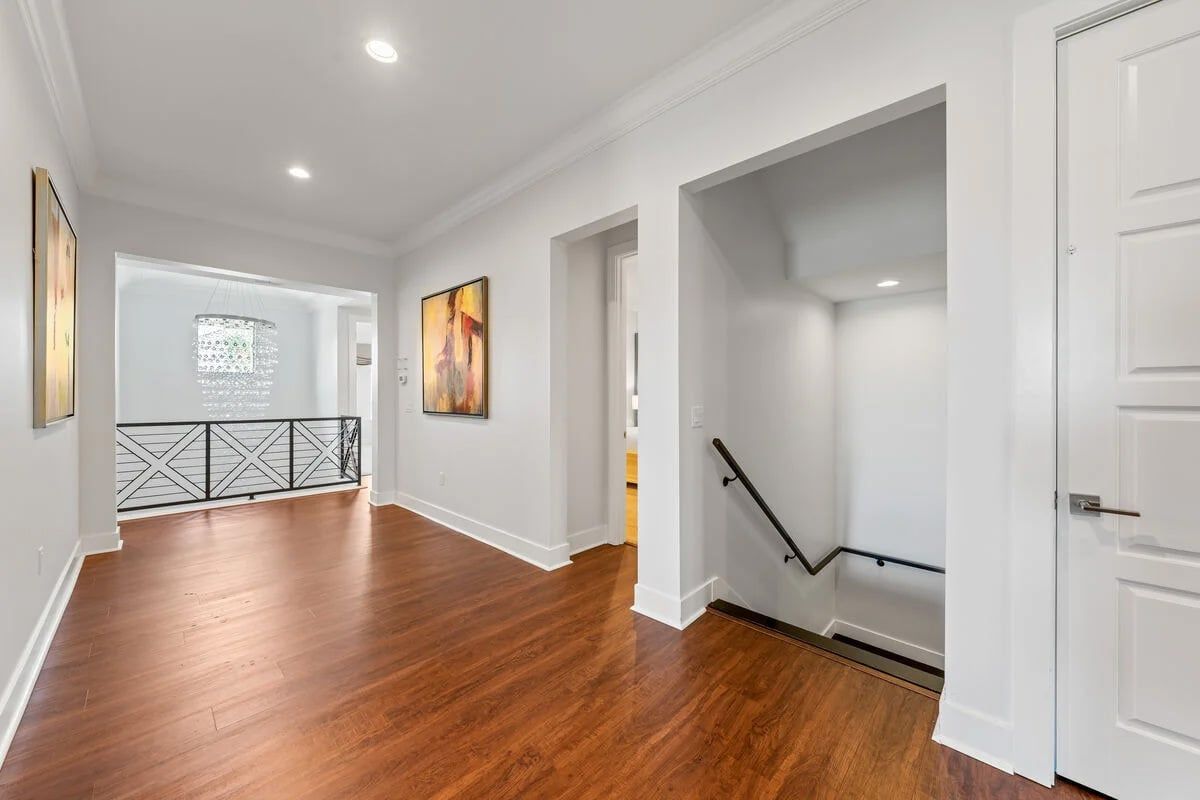 A hallway with wooden flooring, white walls, and a black railing.