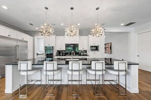 Cocina moderna con una isla central, taburetes de bar, electrodomésticos de acero inoxidable e iluminación colgante.