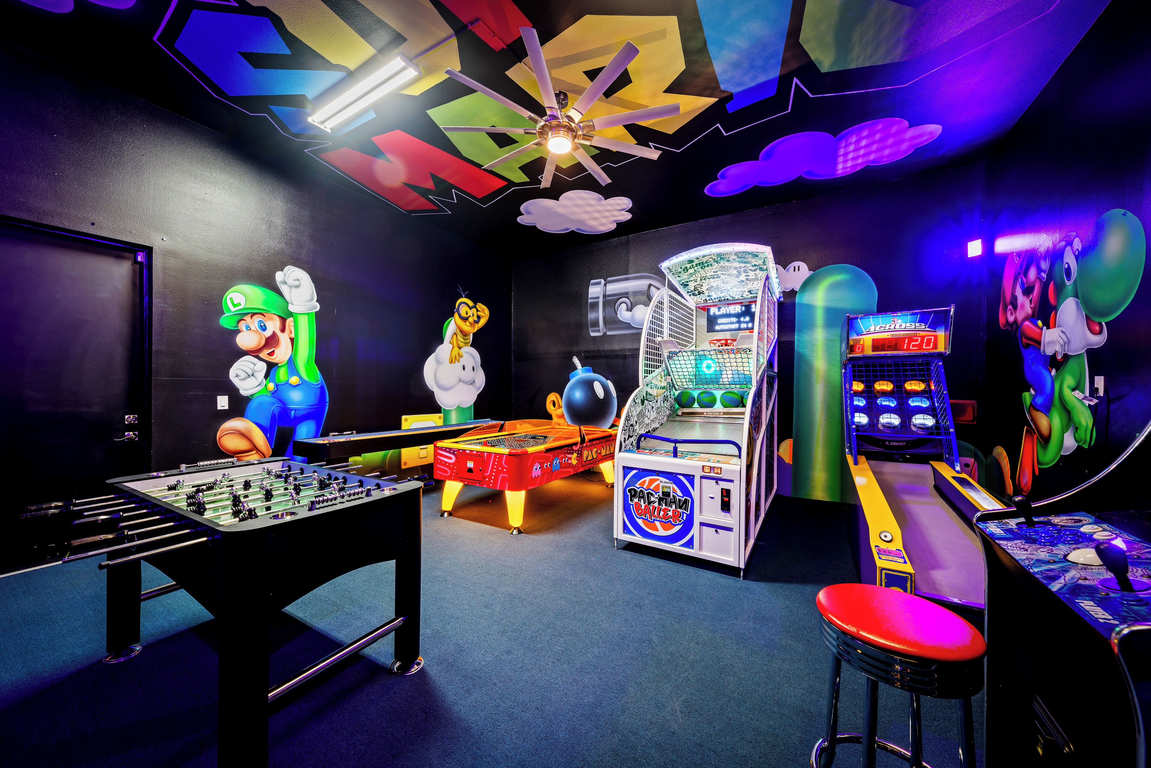 Une pièce équipée d’un baby-foot, d’une borne d’arcade Pac-Man et décorée sur le thème de Mario.