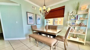 A dining area with a wooden table, cushioned bench, and chairs. There is a chandelier above the table, and a bookshelf with decorative items to the right.