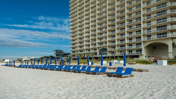 A beach with rows of blue lounge chairs and a large hotel building in the background.