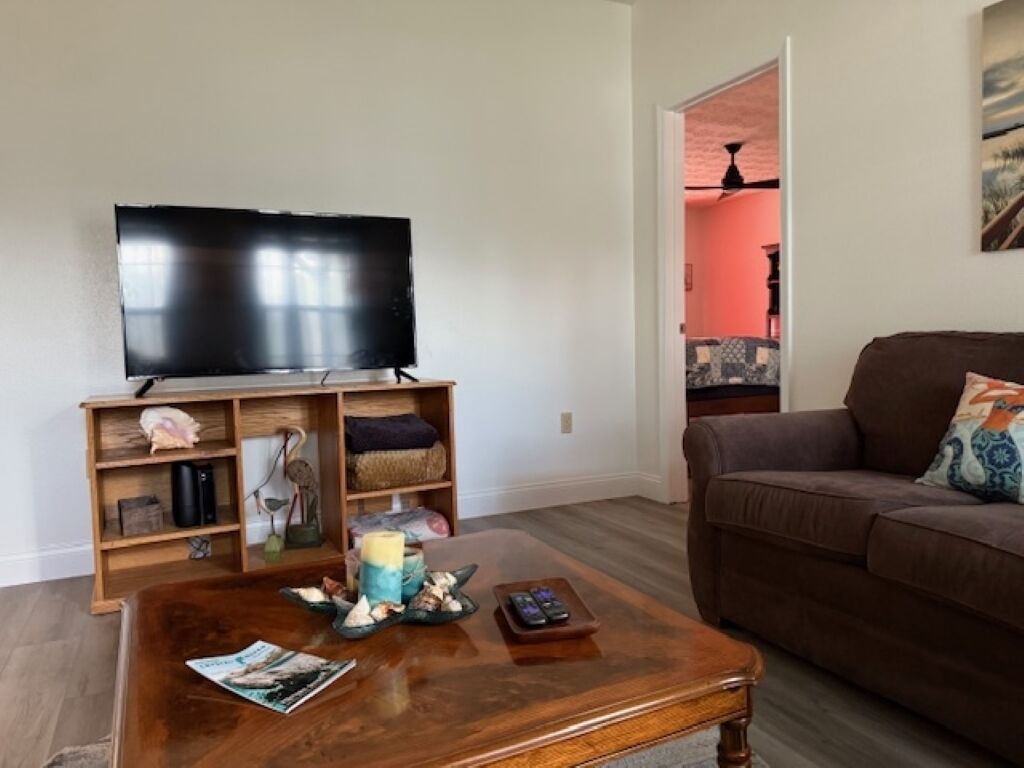Un salon avec un téléviseur à écran plat posé sur un meuble en bois, un canapé en cuir marron et une table basse sur laquelle se trouvent des magazines et une bougie.