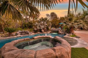 Una piscina circondata da rocce e palme, con una cascata e una piccola vasca idromassaggio.
