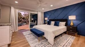 Een moderne slaapkamer met een groot bed, twee nachtkastjes met lampen, een bankje en uitzicht op een waterval door glazen deuren.