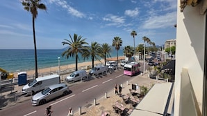 Eine Küstenstraße mit parkenden Autos und einem Bus, Palmen und einem Strand im Hintergrund.