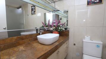 Une salle de bain avec un plan de toilette en marbre, un lavabo blanc, des toilettes et un miroir orné de motifs floraux.