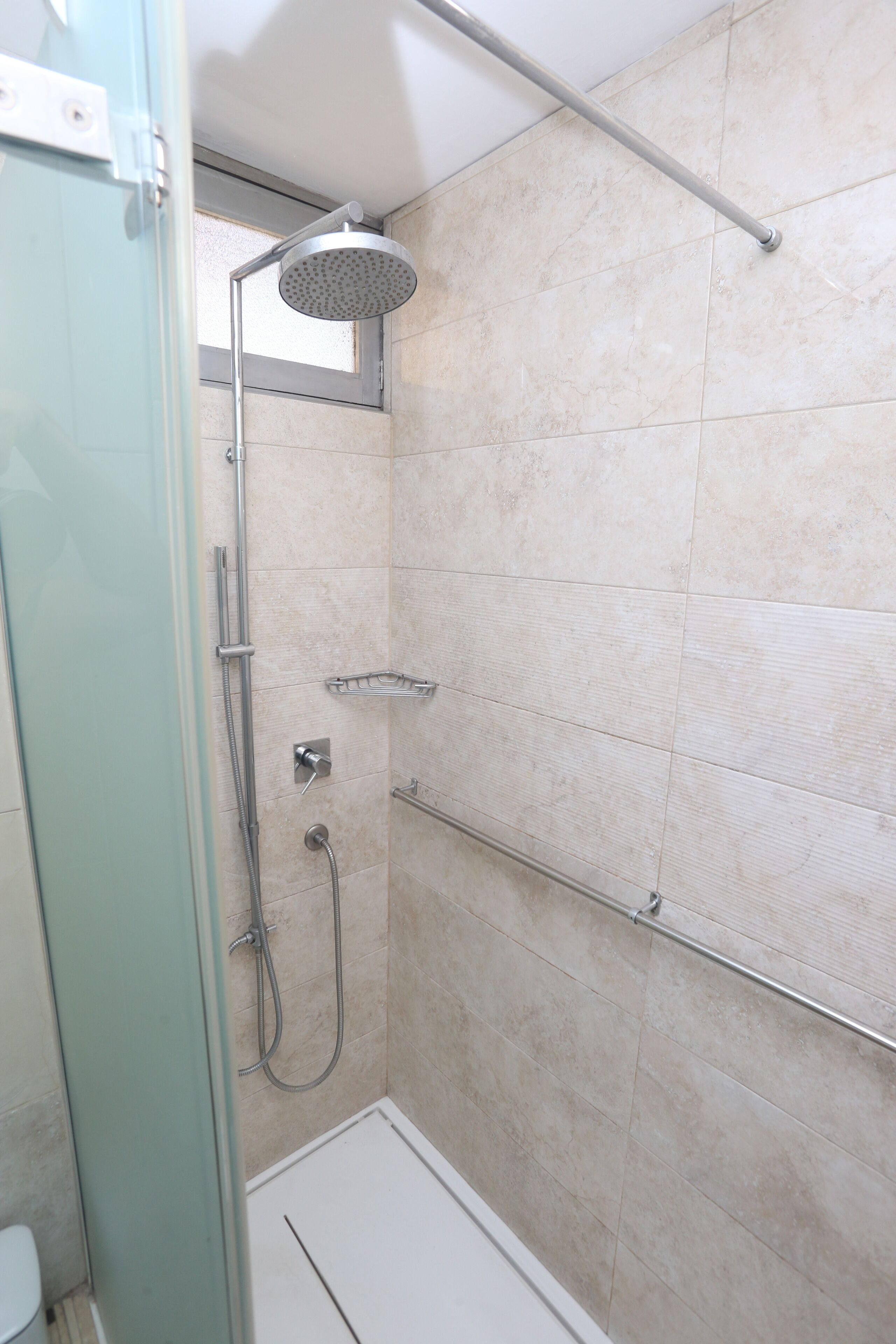 A glass-enclosed shower stall with a handheld showerhead, a handheld shower attachment, and a wall-mounted faucet.