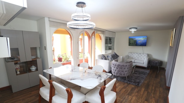 Una sala de estar moderna con comedor, un sofá y un televisor montado en la pared.