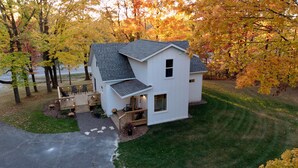A white house with a grey roof, a porch with chairs, and a small deck.