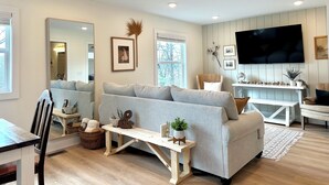 A modern living room with a grey sofa, wooden coffee table, and a flat-screen TV mounted on the wall.