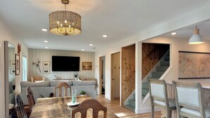 A dining area with a wooden table and chairs, a chandelier, and a staircase leading to another level.