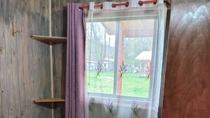 Une chambre avec un mur en bois, une fenêtre ornée d’un rideau violet et un couvre-lit rose matelassé.