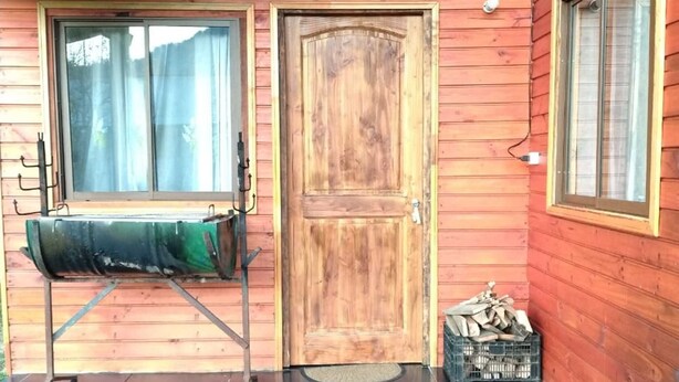 L’entrée d’un chalet en bois, dotée d’une porte coulissante, d’une fenêtre avec un rideau et d’un espace de rangement pour le bois de chauffage.