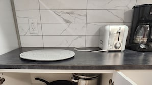 Une cuisine équipée d’un grille-pain, d’une machine à café, d’une casserole et d’un saladier rouge posé sur le plan de travail.