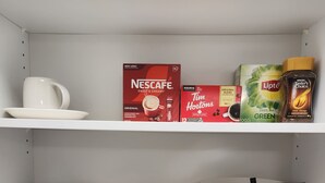 Une étagère de cuisine contenant des produits à base de café et de thé, notamment des boîtes de Nescafe, de Lipton et de Keurig.