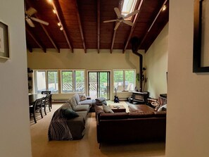 A spacious living room with a high ceiling, large windows, a fireplace, and a dining area.