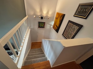 A staircase with a white railing, wooden steps, and a wall with framed artwork.