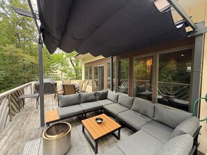 Um terraço ao ar livre com um sofá seccional, uma mesa de madeira e uma lixeira.