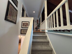 A staircase with a white railing, leading to a landing with framed artwork on the walls.