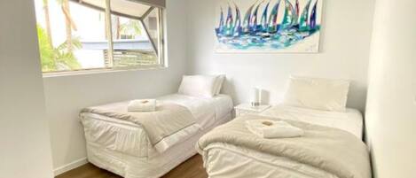 A bedroom with two beds, a ceiling fan, a window with a view, and a painting on the wall.