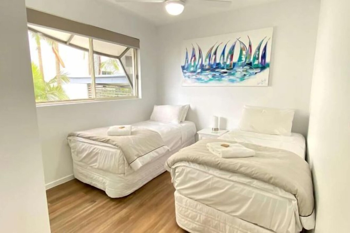 Un dormitorio con dos camas, una ventana y un cuadro de barcos de vela.