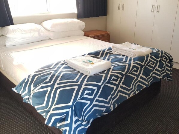 A neatly made bed with a blue and white patterned bedspread, a folded white towel, and a wooden nightstand with a lamp. - Sailfish Cove & RIVA Apartments (Mooloolaba)