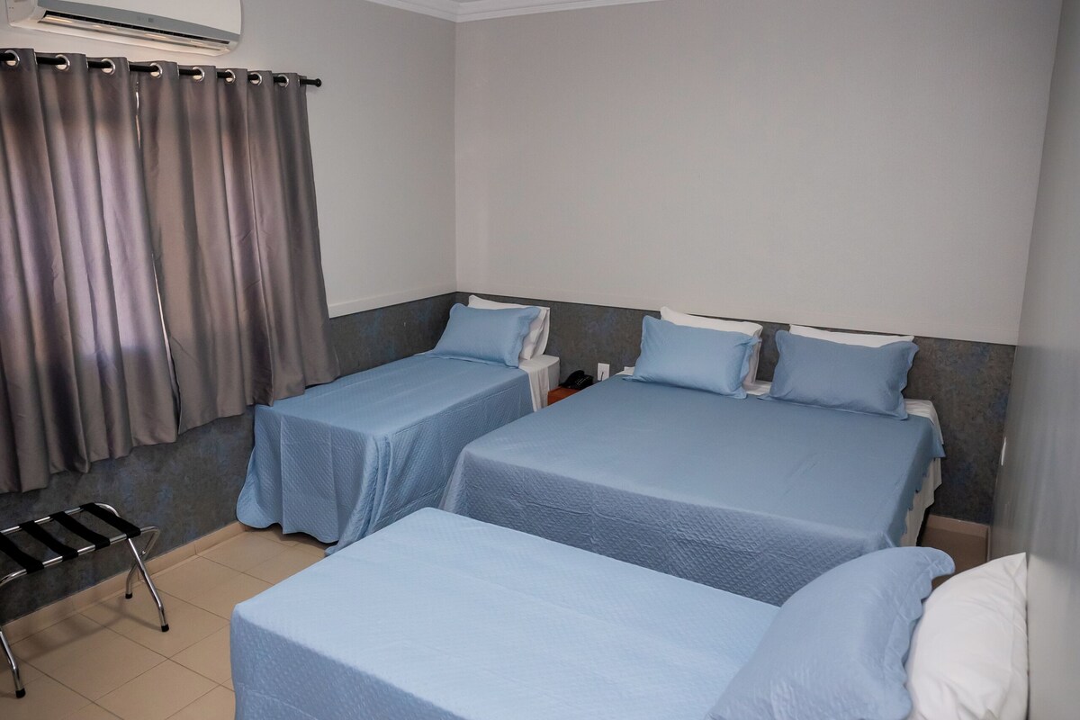 A hotel room with two beds, a desk, an air conditioner, and a ceiling-mounted security camera.