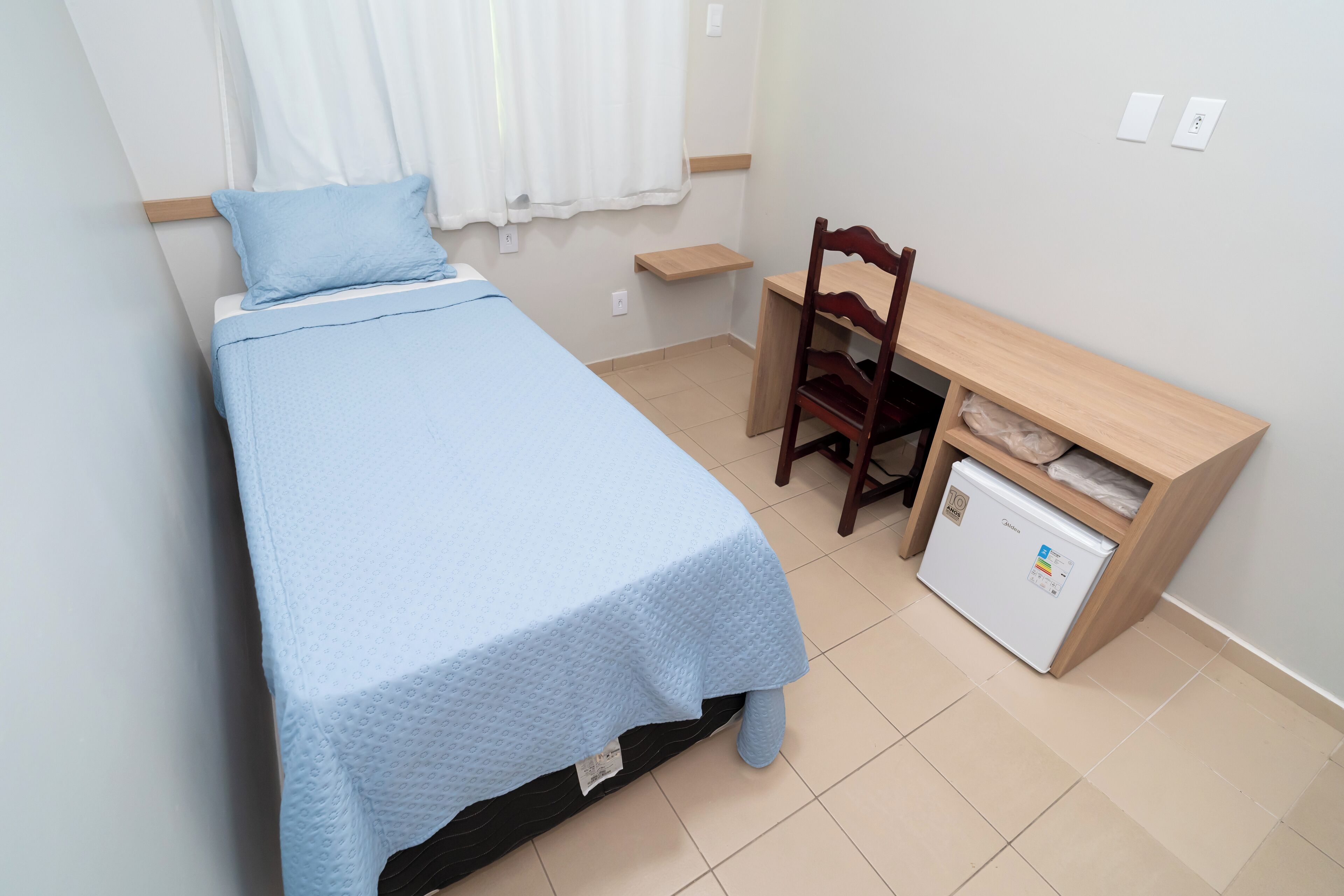 Un dormitorio con una cama, un escritorio de madera, una silla y un refrigerador pequeño.