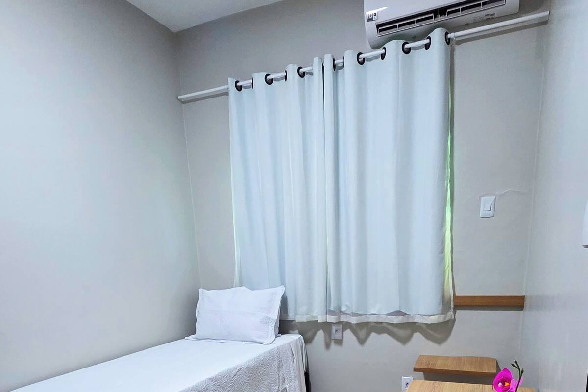 A bedroom with a bed, a desk, a potted plant, and an air conditioning unit.