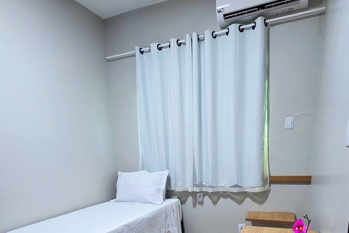 A bedroom with a bed, a desk, a potted plant, and an air conditioning unit.
