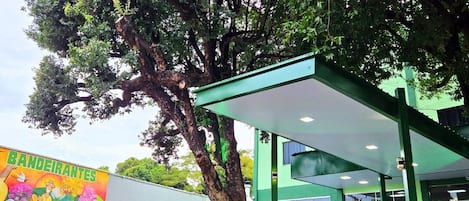 A gas station with a large tree in front, a mural on the wall, and a green building with a covered area.