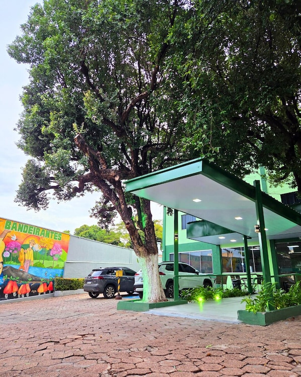 A gas station with a large tree in front, a mural on the wall, and a green building with a covered area.