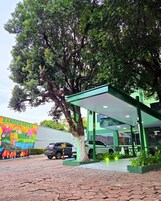 Una estación de servicio con un árbol grande al frente, un mural en la pared y un edificio verde con zona cubierta.
