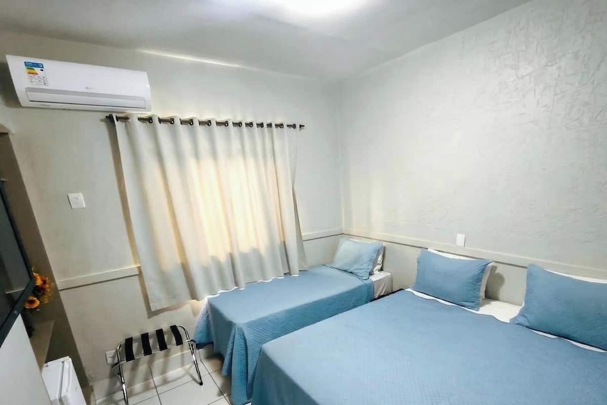 A hotel room with two beds, a window with curtains, an air conditioning unit, and a chair.