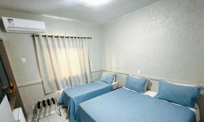A hotel room with two beds, a window with curtains, an air conditioning unit, and a chair. - Bandeirantes Hotel (Cuiaba)