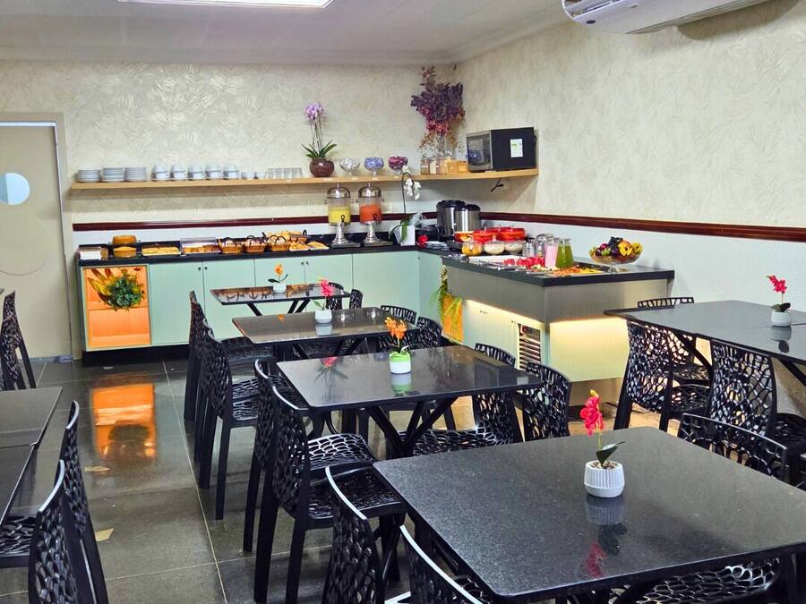 A restaurant interior with black metal chairs and tables, a kitchen counter with various food items, and an air conditioning unit on the ceiling.