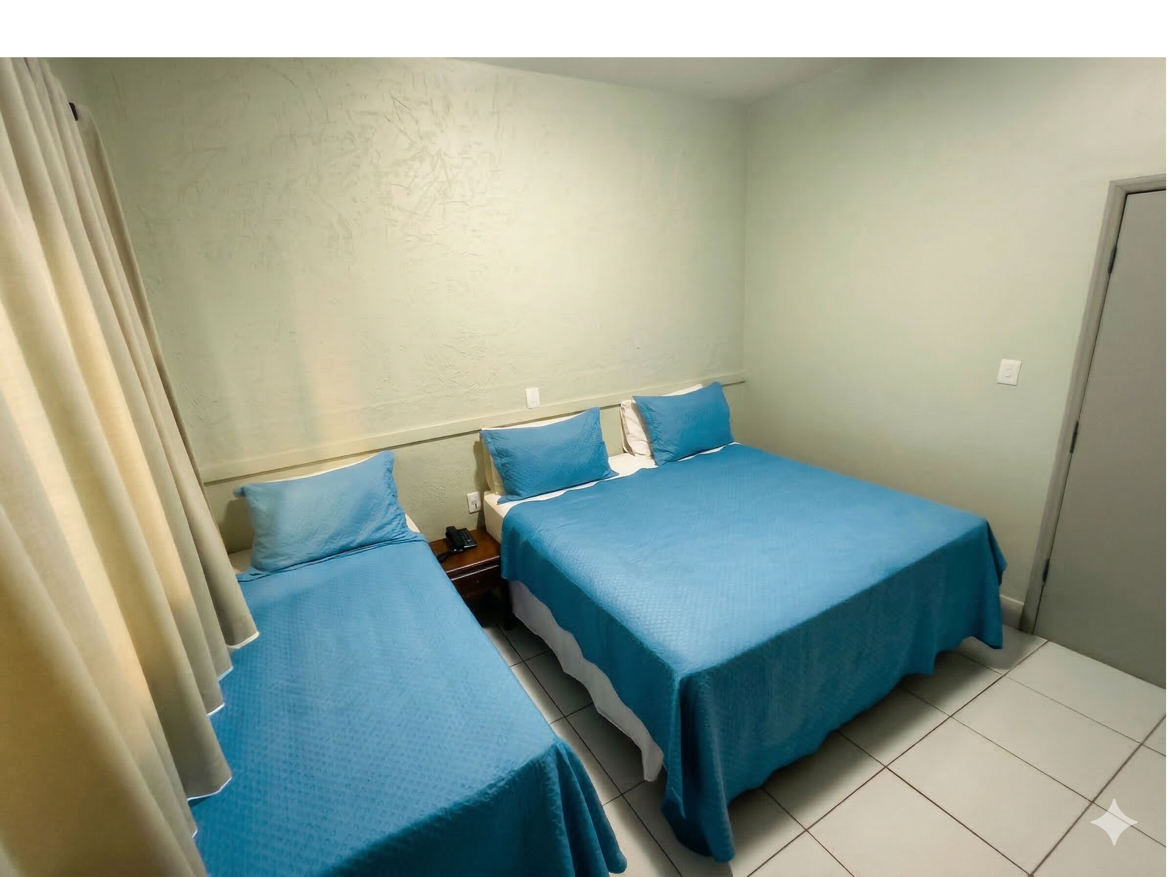 A small, clean room with two single beds, a bedside table with a phone, and a curtain.
