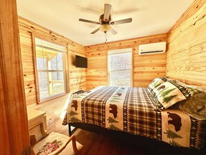A wooden cabin bedroom with a bed, a chair, a desk, and a ceiling fan.